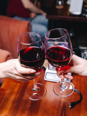 Clinking glasses of red wine on a romantic dinner in a restaurant, close up of hands