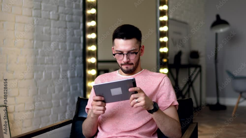 Poster young man lost in online game on modern tablet using home internet connection resting in apartment.h