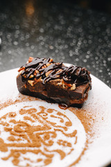 Snickers cake with chocolate topping and crushed nuts on a plate decorated with cocoa powder bar logo