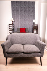 Close up of a loveseat situated at the end of a bed in a modern home. An interesting wallpaper...