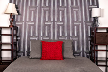 A red pillow on a bed with wallpaper behind.