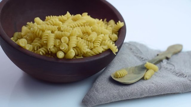 
corkscrew noodles stew falling into wooden bowl with napkin and rustic spoon on white background