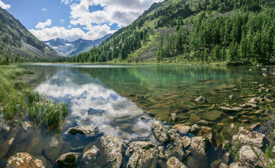 Picturesque mountain lake. Daylight reflected in the water. Forested slopes, stony bottom. Wild place in Siberia.