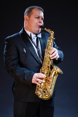Mature Expressive Caucasian Saxophonist in Dark Suit Posing Against Seamless Black Background.