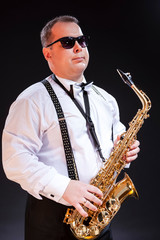 Obraz na płótnie Canvas Mature Caucasian Saxophonist in White Shirt Posing in Sunglasses Against Seamless Black Background.