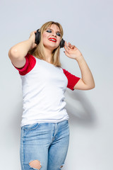 Lifestyle Concepts. Charming Caucasian Girl in White T-Shirt Listening To Music in Headphones. Posing Against White