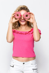 Food Ideas. Portrait of Cute and Funny Caucasian Blond Girl Enjoying Pink Doughnut in Hands. Posing in Sexy Shorts Against White.