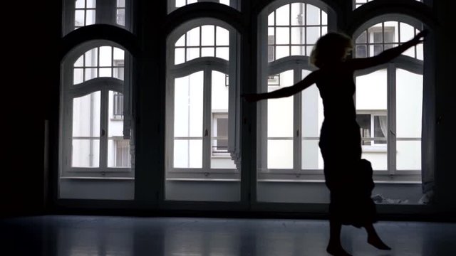 black female silhouette in a long skirt against the background of arched Windows. the woman dances, spreads her arms, spins, jumps. the camera is moving