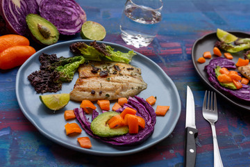 Fish with vegetables, purple cabbage, red bell pepper, shadow on a blue background, for summer