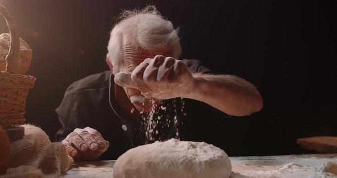 Professional mature caucasian baker putting flour on loaf of bread dough with passion, retired pensioneer enjoying his new hobby, isolated on black background 4k footage