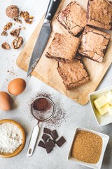 Top view of freshly baked home made brownie cake arranged with recipe ingredients over white rustic background.