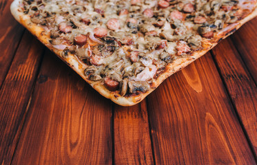 Homemade fresh pizza with sausages, mushrooms, cheese and onions lies on a mahogany wooden table....