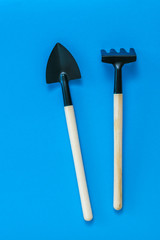 Rake and shovel for cultivating soil on a blue background.