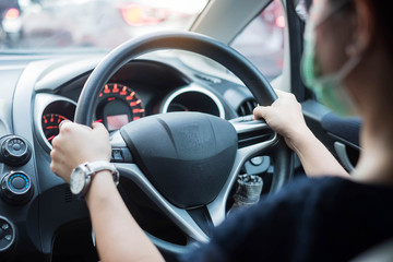 Young woman wearing protective face mask and hand controlling steering wheel in her car, against coronavirus or Corona Virus Disease (Covid-19). personal Hygiene lifestyle and New Normal concept