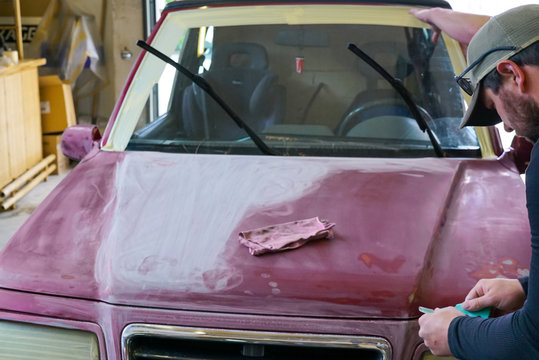 close up view of a man' sanding the hood of a truck before a paint job