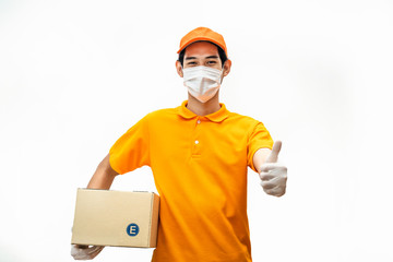 Fototapeta na wymiar Asian deliver man wearing face mask in orange uniform holding box of food, groceries gives thumbs up standing in white isolated background. Postman and express delivery service during covid19 pandemic