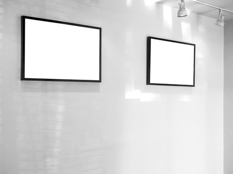 Two white blank frames on white wall background.