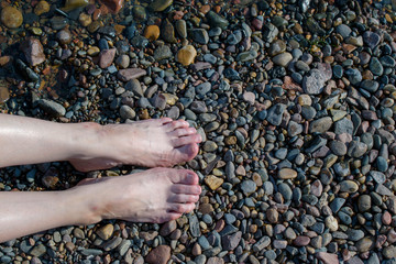 Female tired legs on a rocky beach. Pebbles, water. After a long walk, calluses, scuffs, scratches, painful corns. Concept of vacation in travel, camping trip.