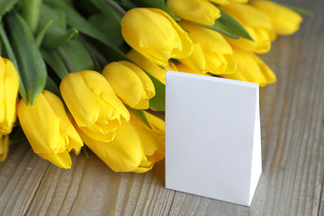 gift and flowers . a white box with space for text on a background of yellow tulips on a gray Board with a wood texture.