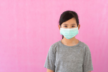 Little asian girl wearing sterile medical mask for protect Covid-19 isolated on pink background....