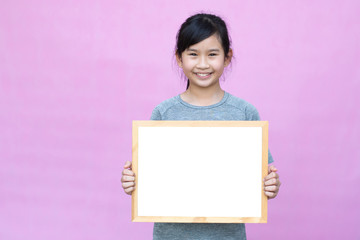 Little asian girl holding whiteboard isolated on pink background.