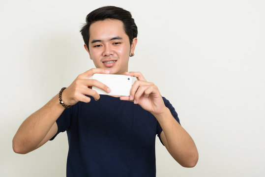 Portrait of happy young Asian man taking picture with phone