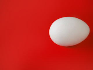 an entire unpainted white egg lies on a rich red background