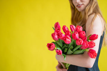 Naklejka premium Unrecognizable woman with a bouquet of red tulips on a yellow background. A girl in a black dress holds an armful of flowers. A gift for International Women's Day. Spring holiday.