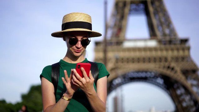 Slow motion of hipster girl in sunglasses walking near Eiffel Tower enjoying trip and making photo on smartphone to share in social networks.Tourist travelling in urban setting of Paris
