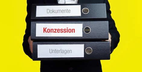 Konzession. Mann im Anzug trägt einen Stapel Aktenordner. Hintergrund gelb. Ein Ordner hat eine...