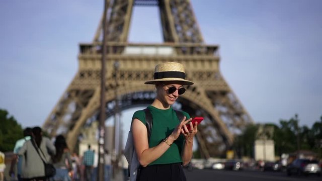 Slow motion of young woman tourist walking on street of Paris near Eiffel Tower and making photos on smartphone enjoying trip on weekend.Hipster traveler taking picture on mobile phone 
