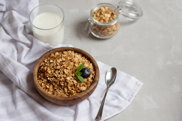 Top view on a wooden bowl with freshly prepared granola or oatmeal granola and a glass of milk nearby. Healthy breakfast at home for children