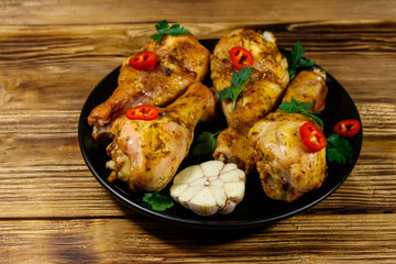 Roasted chicken drumsticks with spices in a black plate on a wooden table