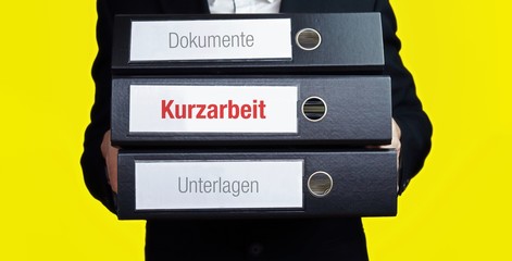 Kurzarbeit. Mann im Anzug trägt einen Stapel Aktenordner. Hintergrund gelb. Ein Ordner hat eine...