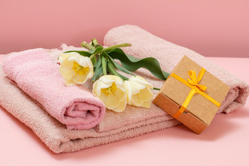 Gift box, towels with tulip flowers on a pink background.