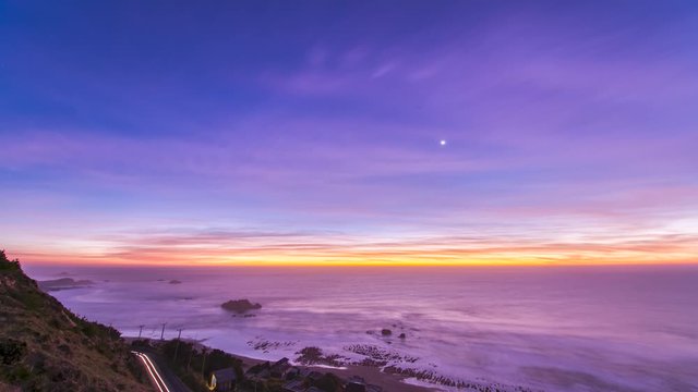 An idyllic scenery at Matanzas beach, the waves coming from the Pacific Ocean illuminated by a moody sky during twilight. Amazing sea landscape with a colorful sky and a small waxing crescent Moon
