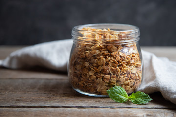 A glass jar with homemade granola or granola made from oat and sweet cereal, decorated with mint...