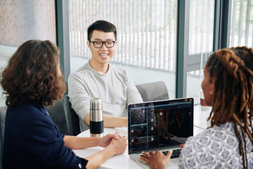 Young Asian man meeting with professional stock market traiders in office and asking for advice