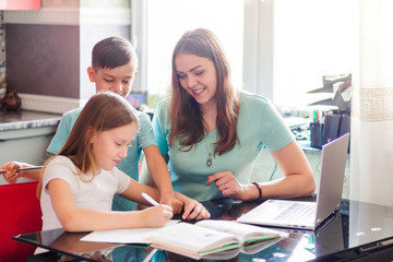 Obraz premium Mom and daughter doing school lessons together looking at a laptop monitor. Boy, little brother stands behind and watches