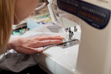 woman in glasses sews on modern sewing machine