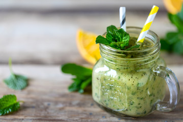 Homemade green smoothie in a jar with spinach, orange, apple and mint in glass jar and ingredients. Detox, diet, healthy, vegetarian food concept. Copy space
