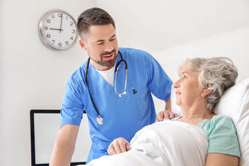 Male doctor working with elderly patient in hospital room