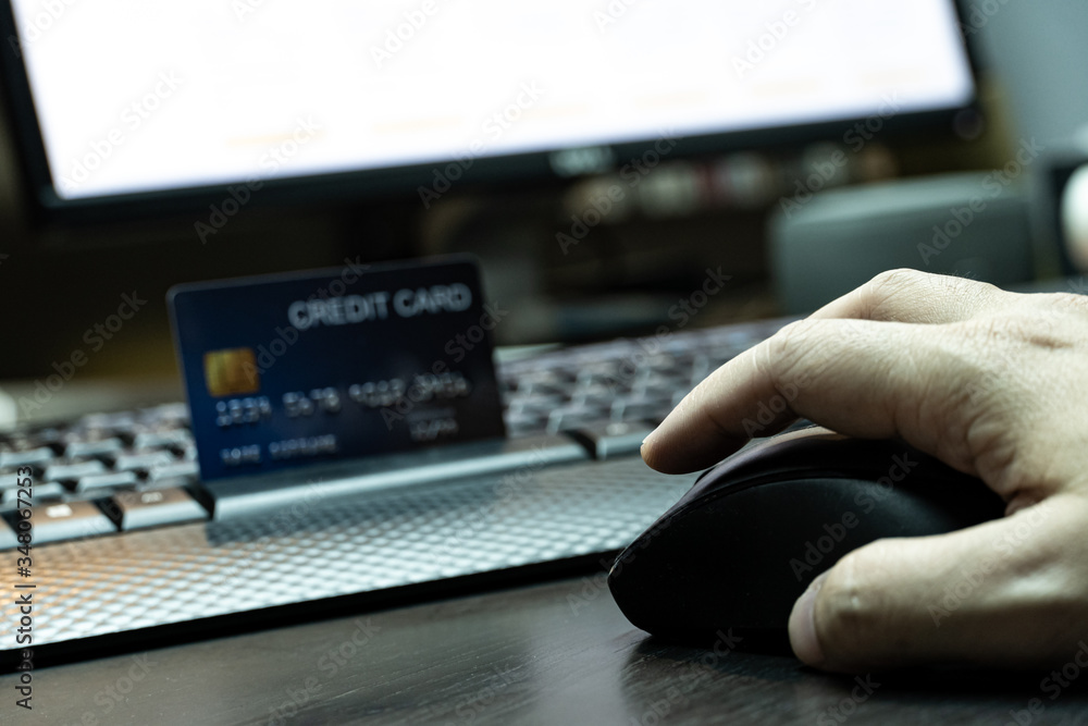 Poster close up Shallow focus hand hold mouse with credit card and Computer background. Background for E-commerce and online shopping concept.