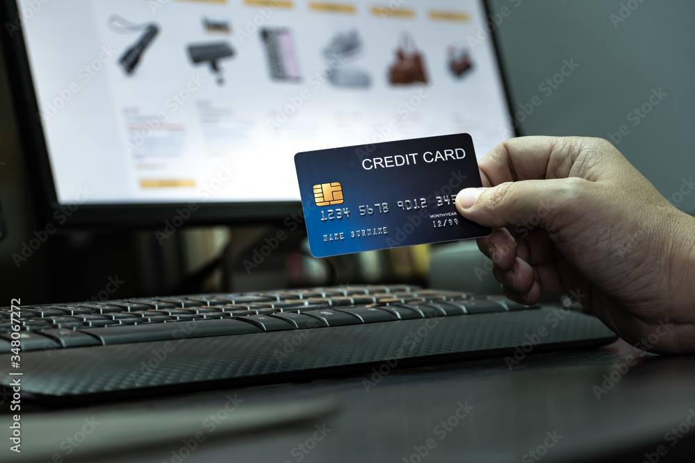 Aufkleber close up Shallow focus hand hold Credit Card on Computer keyboard and E-commerce website on monitor background. Background for E-commerce and online shopping concept.