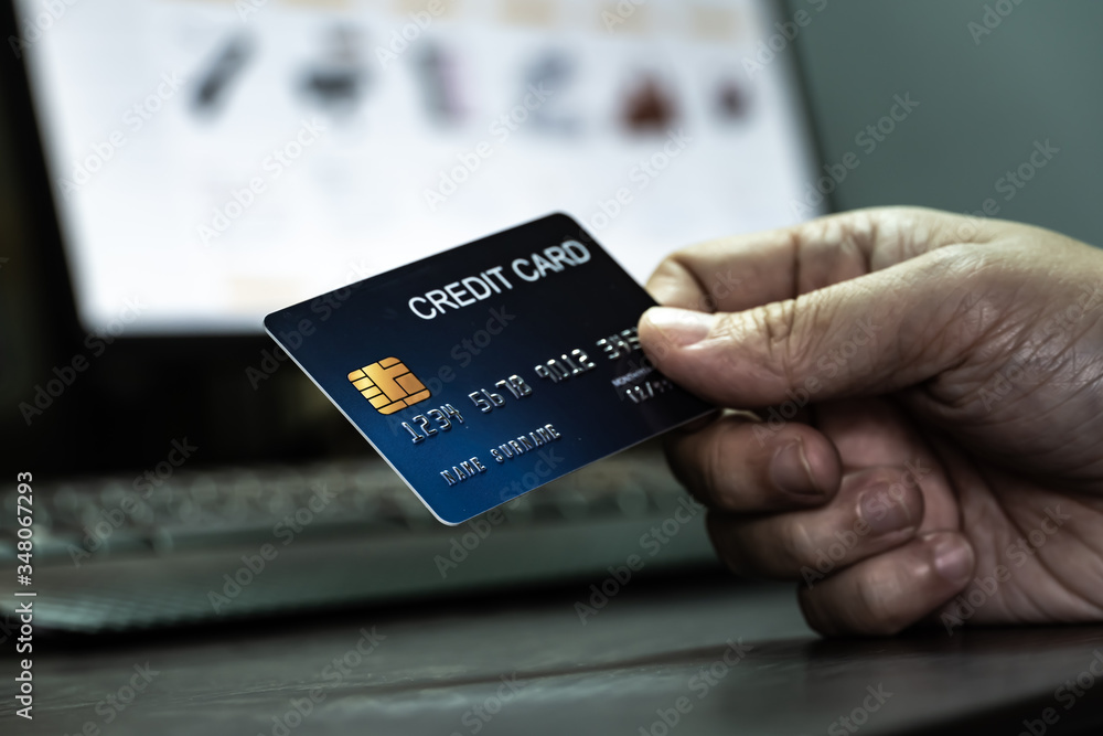 Poster close up Shallow focus hand hold Credit Card on Computer keyboard and E-commerce website on monitor background. Background for E-commerce and online shopping concept.