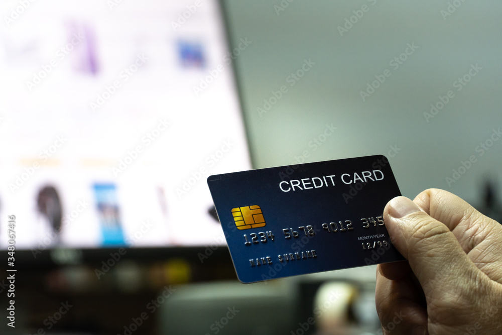 Poster close up Shallow focus hand hold Credit Card with Computer keyboard and E-commerce website on monitor background. Background for E-commerce and online shopping concept.