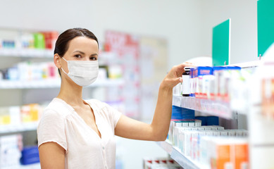 medicine, healthcare and people concept - female customer in face protective medical mask for protection from virus disease choosing drugs at pharmacy