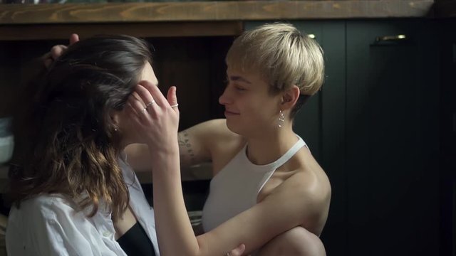 Affectionate cute nice lesbian couple hugging and kissing while sitting on kitchen floor spbd. beautiful young girls talking with smile. romantic relationship, same sex woman concept