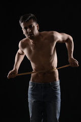 Fototapeta na wymiar Sick man measuring his waist on dark background. Concept of anorexia
