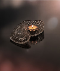 Still life studio photo of a crystal heart with a lit candle inside.  Back lit on a reflective surface